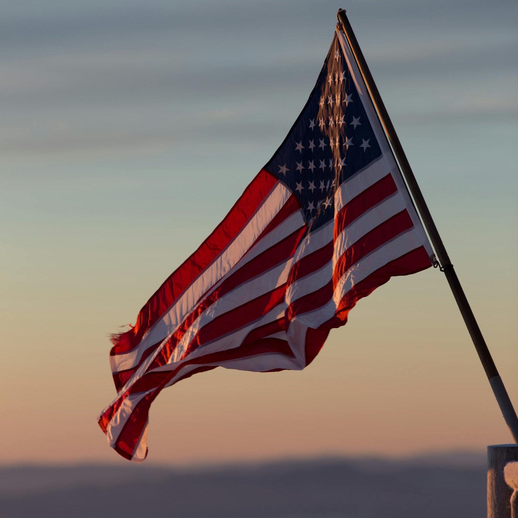 A vibrant US flag waves against a scenic sunset backdrop in Stowe, Vermont.