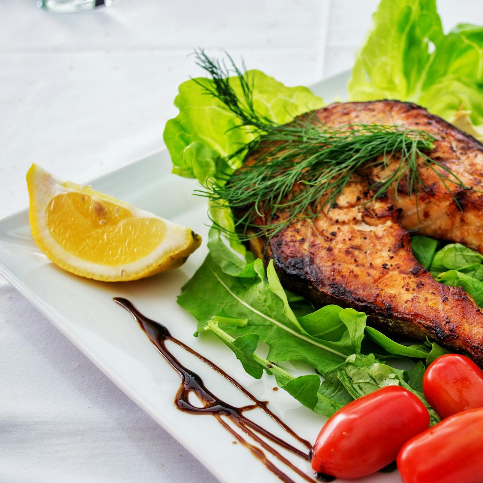 Delicious grilled salmon steak served with avocado, lettuce, cherry tomatoes, and lemon slice on a white plate.